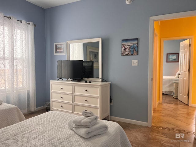 bedroom featuring connected bathroom, light tile flooring, and multiple windows
