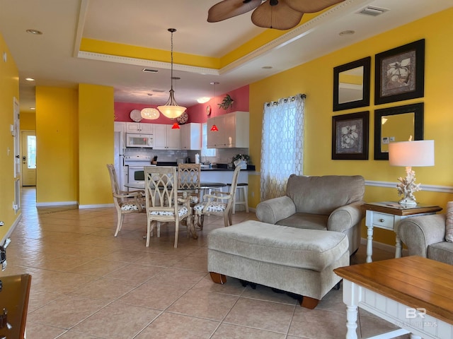 living room with ceiling fan, light tile floors, and a raised ceiling