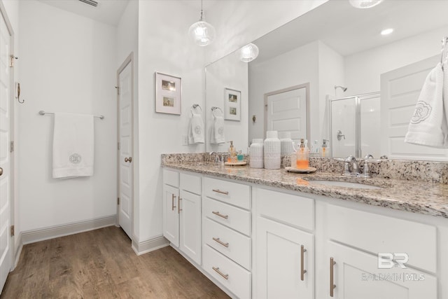 full bath featuring a stall shower, double vanity, a sink, and wood finished floors