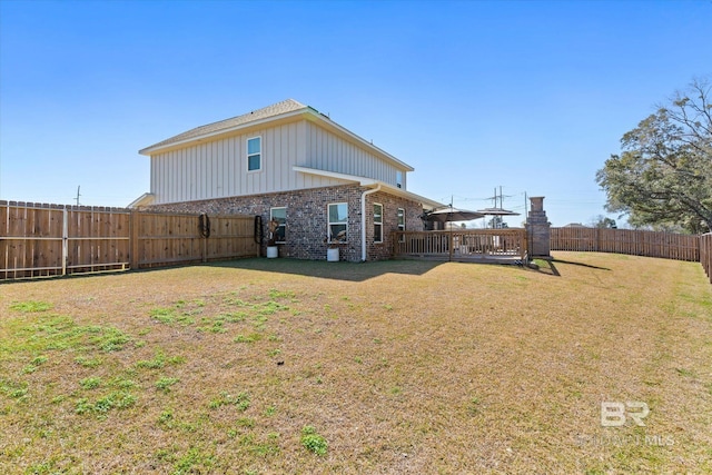 rear view of house with brick siding, a yard, a fenced backyard, and a wooden deck