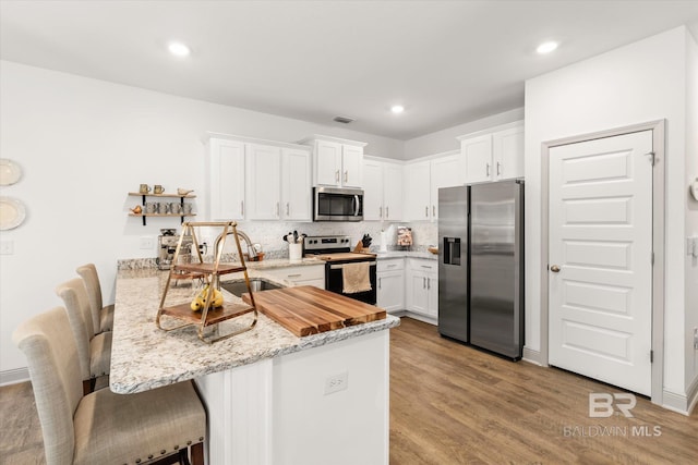 kitchen with visible vents, white cabinets, appliances with stainless steel finishes, a peninsula, and a sink