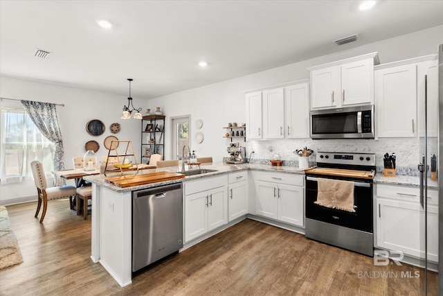 kitchen with visible vents, white cabinets, appliances with stainless steel finishes, a peninsula, and a sink