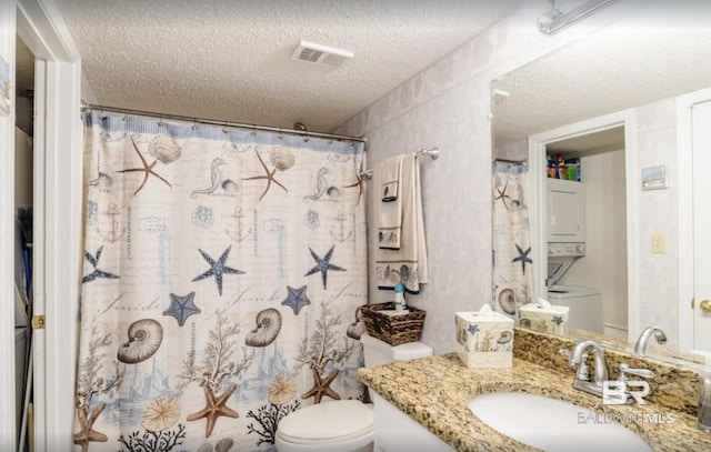 bathroom featuring a textured ceiling, toilet, vanity, visible vents, and stacked washing maching and dryer