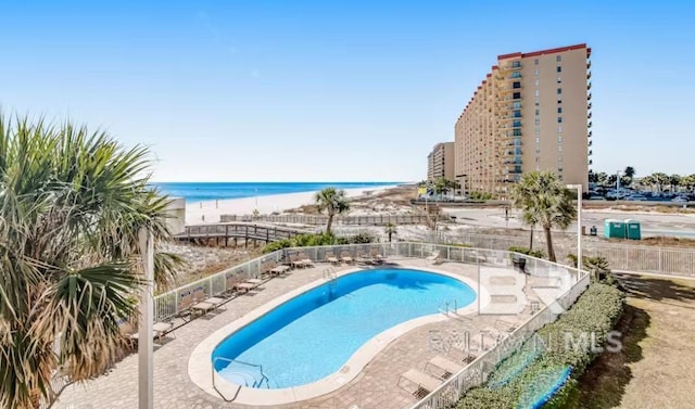 pool featuring a patio area, a water view, fence, and a beach view