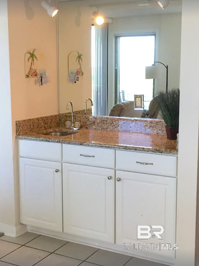 kitchen with light tile patterned floors, dark stone countertops, a sink, and white cabinetry