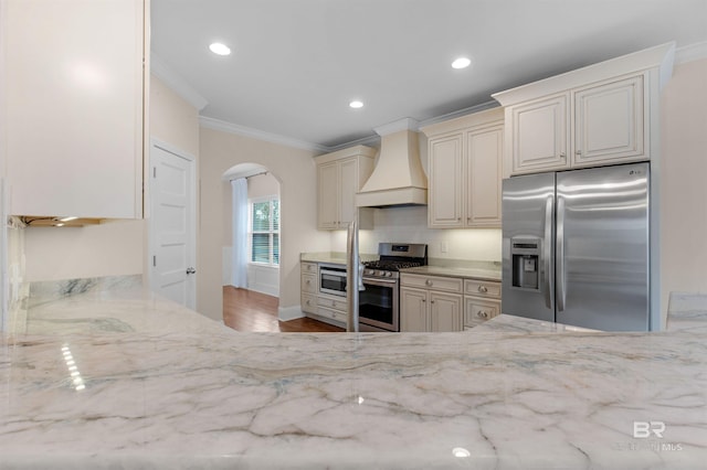 kitchen featuring light stone counters, ornamental molding, stainless steel appliances, and custom range hood