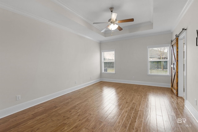 empty room with hardwood / wood-style flooring, crown molding, ceiling fan, a barn door, and a raised ceiling