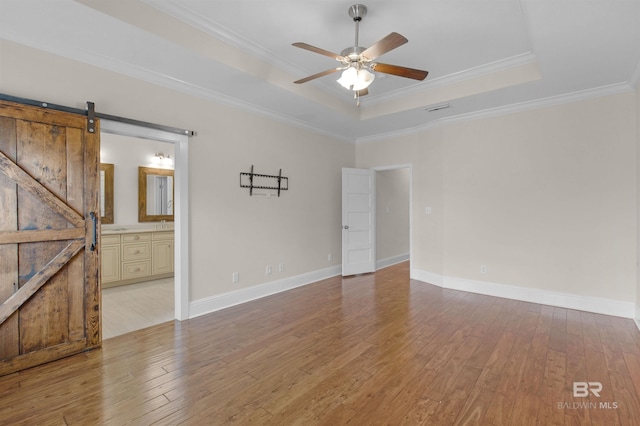 spare room with ornamental molding, a barn door, a raised ceiling, and light wood-type flooring