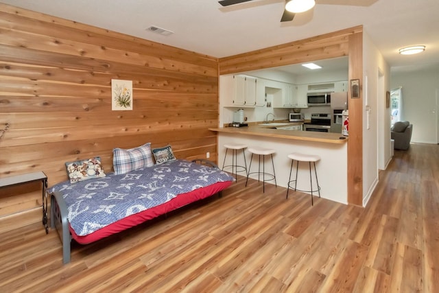 bedroom with wooden walls, refrigerator, sink, and light hardwood / wood-style flooring