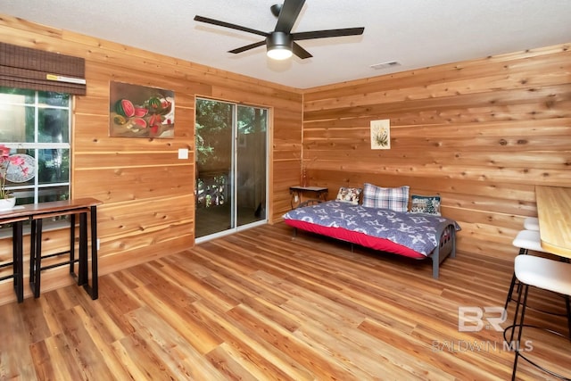 bedroom with ceiling fan, wood walls, and light hardwood / wood-style floors