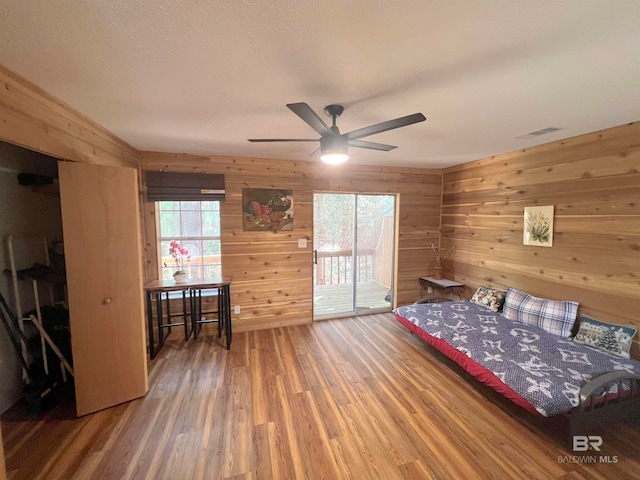 bedroom with access to exterior, wooden walls, ceiling fan, and dark wood-type flooring