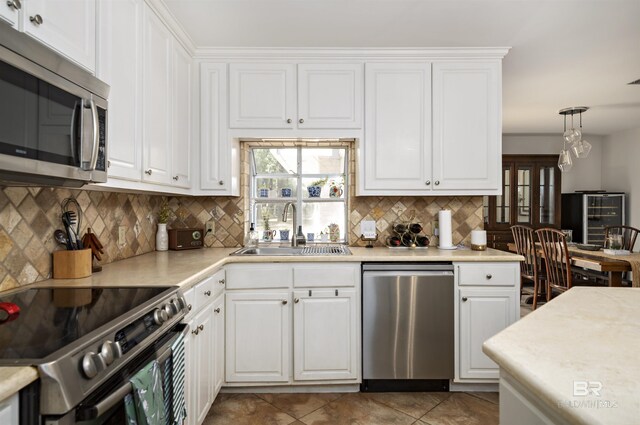 kitchen featuring light countertops, decorative backsplash, white cabinets, stainless steel appliances, and a sink