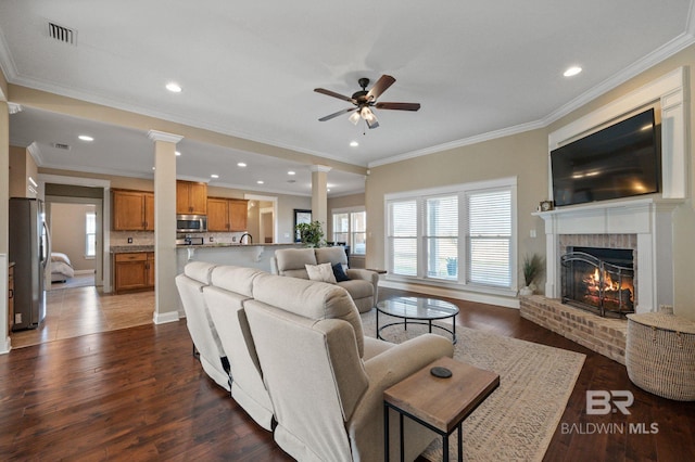 living room featuring a healthy amount of sunlight, a fireplace, dark hardwood / wood-style flooring, and decorative columns