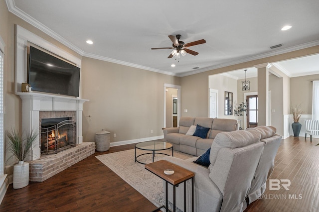 living room featuring crown molding, dark wood-type flooring, ceiling fan, and a fireplace