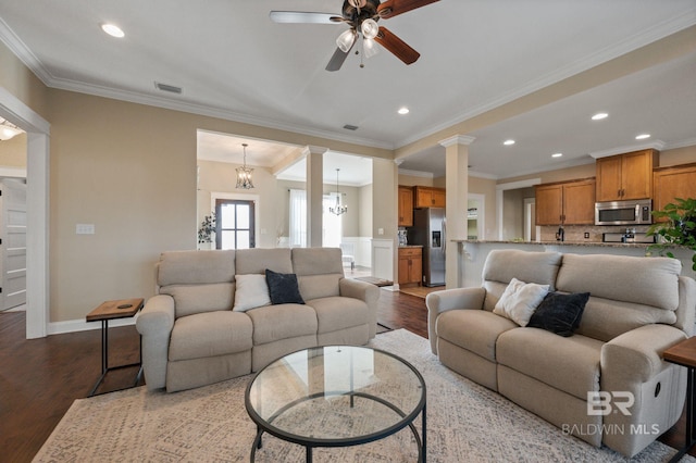 living room featuring ceiling fan with notable chandelier, ornamental molding, wood-type flooring, and decorative columns