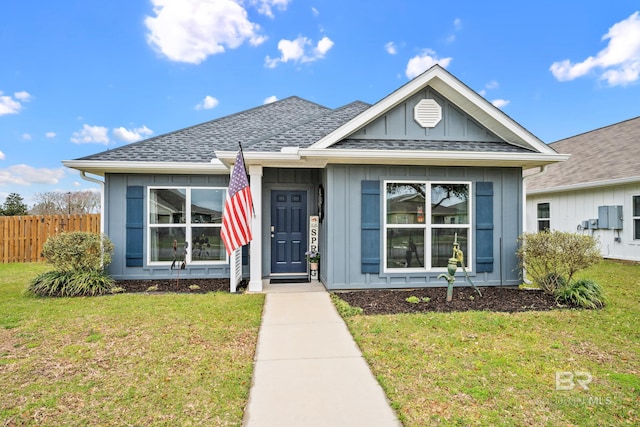 bungalow-style home featuring roof with shingles, board and batten siding, a front lawn, and fence