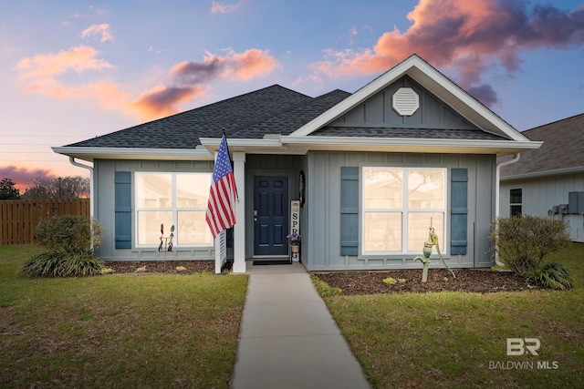 single story home featuring a yard, board and batten siding, roof with shingles, and fence