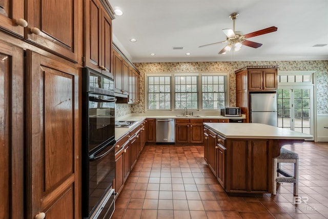 kitchen with wallpapered walls, a kitchen island, appliances with stainless steel finishes, brown cabinets, and light countertops