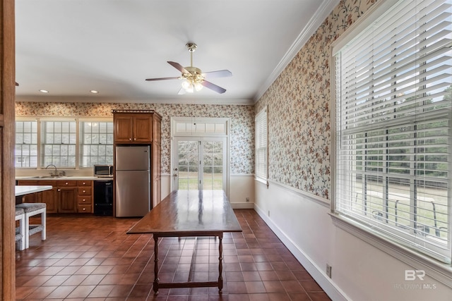 kitchen featuring a wainscoted wall, light countertops, appliances with stainless steel finishes, brown cabinets, and wallpapered walls