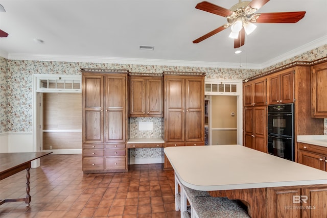kitchen featuring dobule oven black, wallpapered walls, brown cabinetry, light countertops, and a kitchen bar