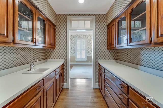 kitchen featuring glass insert cabinets, brown cabinets, light countertops, and a sink