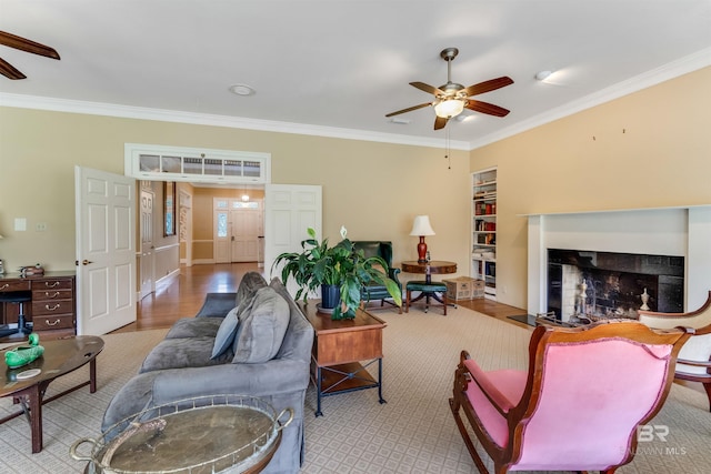 living room with built in shelves, a fireplace, ornamental molding, and a ceiling fan
