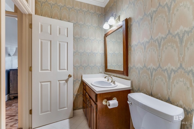 half bathroom featuring tile patterned flooring, toilet, vanity, ornamental molding, and wallpapered walls