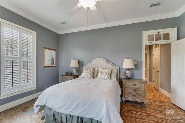 bedroom featuring ornamental molding, wood finished floors, visible vents, and baseboards