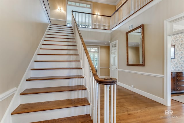 staircase featuring a towering ceiling, wood finished floors, visible vents, and baseboards