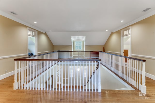 interior space with wood finished floors, visible vents, baseboards, vaulted ceiling, and ornamental molding