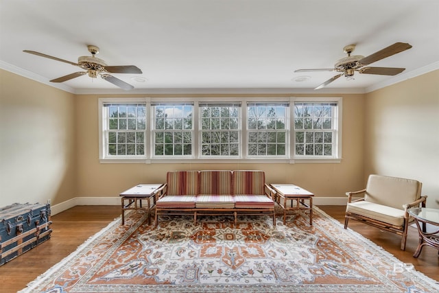 living area featuring baseboards, wood finished floors, a ceiling fan, and crown molding