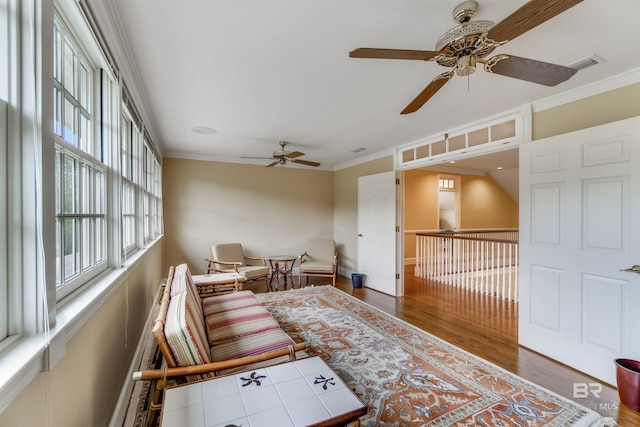 living area featuring baseboards, visible vents, ornamental molding, and wood finished floors