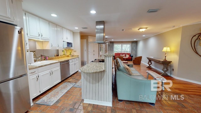 kitchen with island exhaust hood, appliances with stainless steel finishes, light stone counters, white cabinets, and a kitchen island