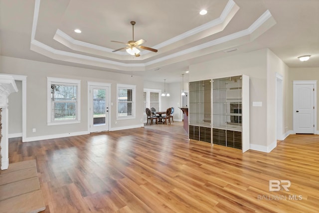 unfurnished living room with crown molding, a tray ceiling, a fireplace, and wood-type flooring