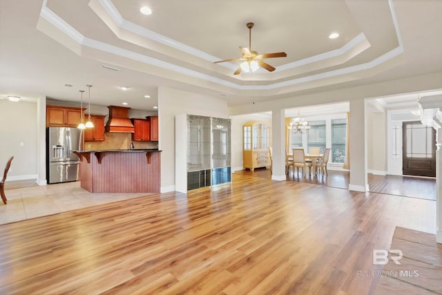 unfurnished living room featuring crown molding, a tray ceiling, light hardwood / wood-style flooring, and ceiling fan with notable chandelier