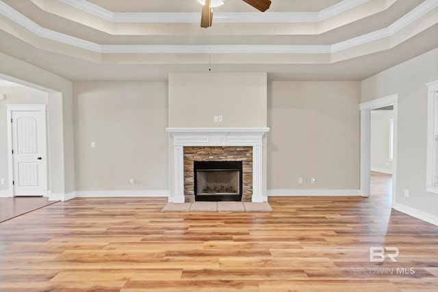 unfurnished living room featuring ceiling fan, a tray ceiling, a stone fireplace, and light hardwood / wood-style flooring