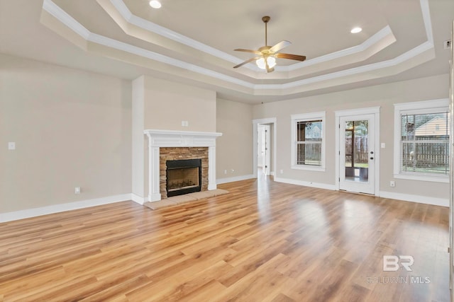 unfurnished living room with a fireplace, ornamental molding, ceiling fan, a raised ceiling, and light hardwood / wood-style flooring