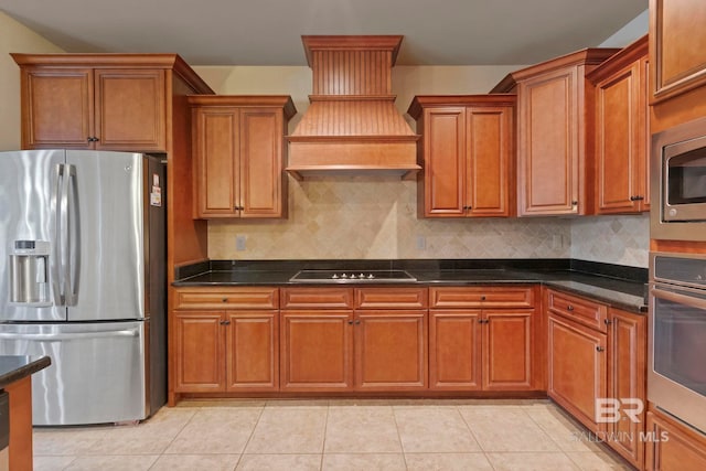 kitchen with stainless steel appliances, custom range hood, light tile patterned floors, and dark stone counters