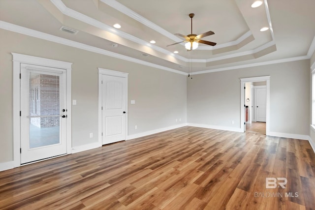 empty room with hardwood / wood-style flooring, ceiling fan, ornamental molding, and a tray ceiling