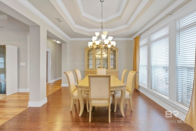 dining room featuring hardwood / wood-style flooring, ornamental molding, a raised ceiling, and a notable chandelier