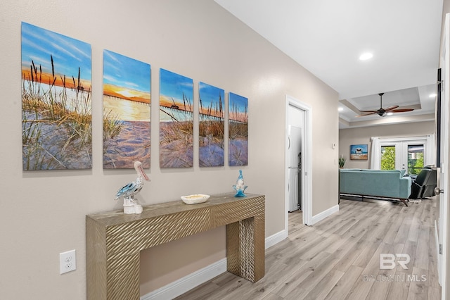 hall with baseboards, a raised ceiling, french doors, light wood-style floors, and recessed lighting