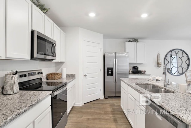 kitchen with stainless steel appliances, light wood-type flooring, white cabinets, a sink, and recessed lighting