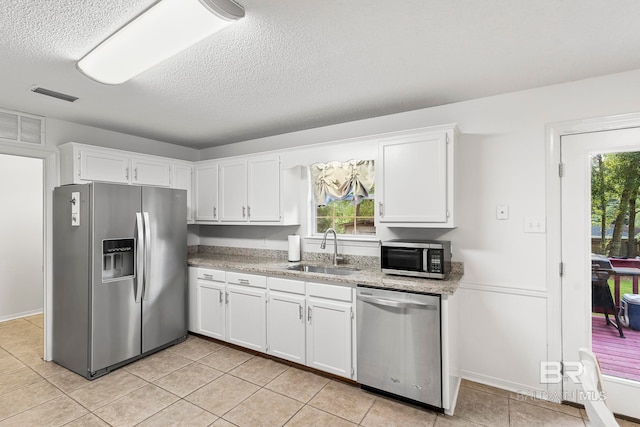 kitchen with a textured ceiling, stainless steel appliances, sink, white cabinets, and light tile patterned flooring