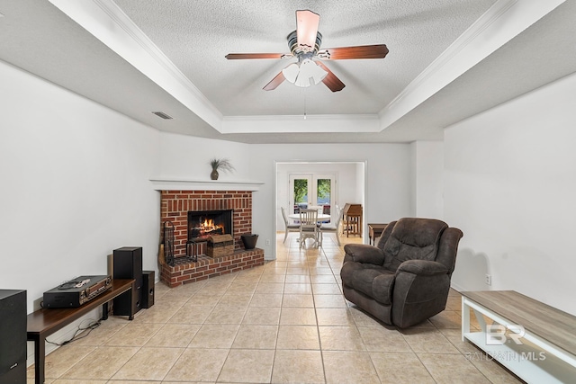 living room with a fireplace, a textured ceiling, ceiling fan, a raised ceiling, and light tile patterned flooring