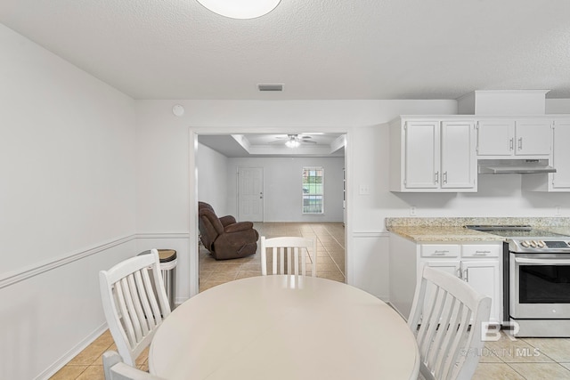 tiled dining area with a textured ceiling, ceiling fan, and a tray ceiling