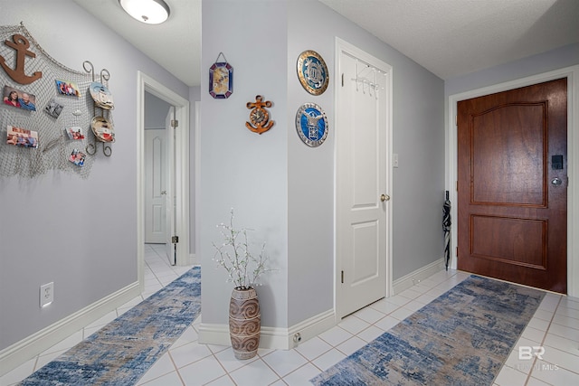 foyer entrance with light tile patterned floors, a textured ceiling, and baseboards
