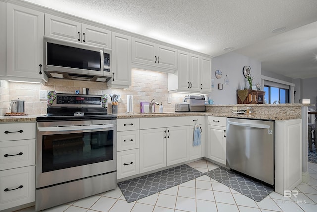 kitchen with tasteful backsplash, a peninsula, white cabinets, appliances with stainless steel finishes, and a sink