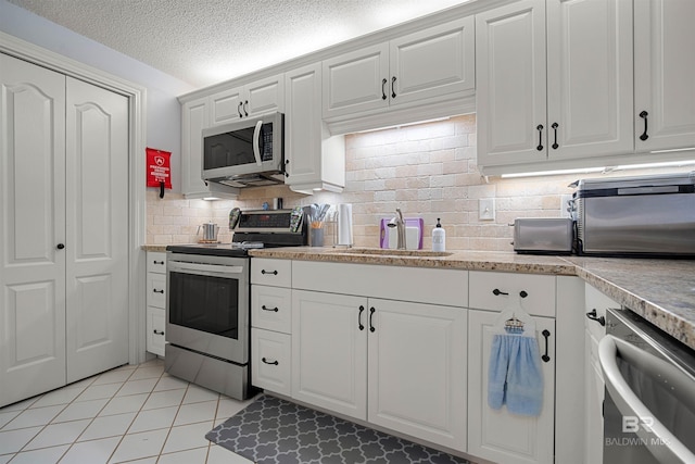 kitchen featuring tasteful backsplash, white cabinets, appliances with stainless steel finishes, light tile patterned flooring, and a sink