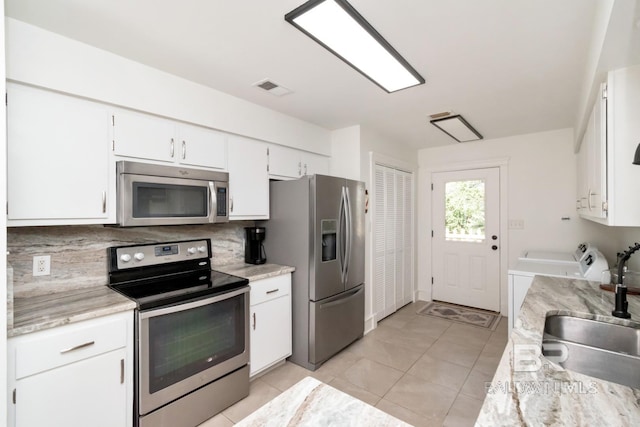 kitchen with light tile patterned flooring, sink, white cabinetry, stainless steel appliances, and washer and clothes dryer