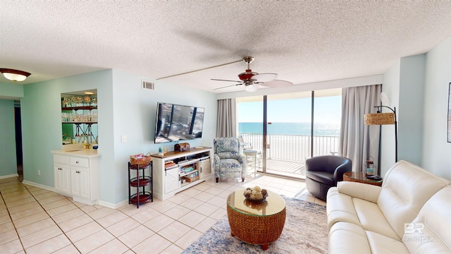 tiled living room with ceiling fan, a wall of windows, and a textured ceiling